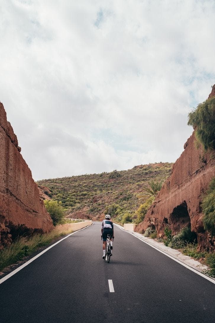 A lone cyclist riding a quiet road where it cuts between low walls of exposed rock.
